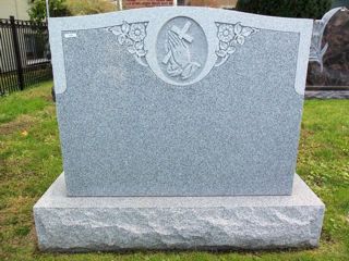 Gray granite monument with hands holding cross within oval and flowers on either side