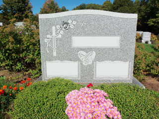 Gray granite double memorial with cross and flower in upper left corner and interlocked wedding bands in center between name areas