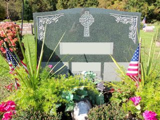 Gray granite memorial with celtic cross, flowers at upper corners, and space for three text spaces