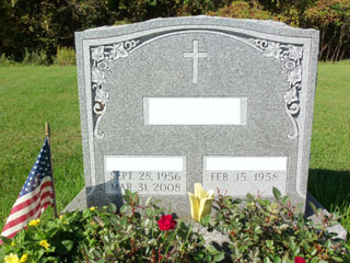 Gray granite memorial with single cross, flowers at upper corners, and space for two names